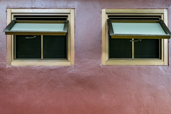 Two open awning windows on a red wall